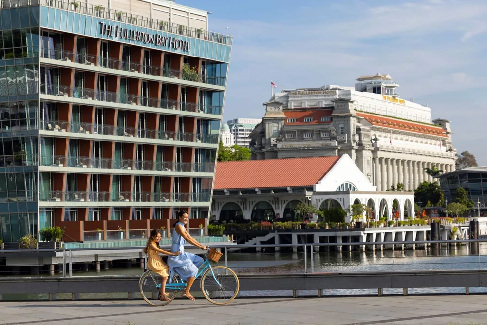 Cyclists on the Marina Bay waterfront in front of The Fullerton Hotel Singapore and The Fullerton Bay Hotel