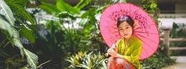 Child in Peranakan kebaya with a pink parasol in the gardens of Shangri-La Singapore
