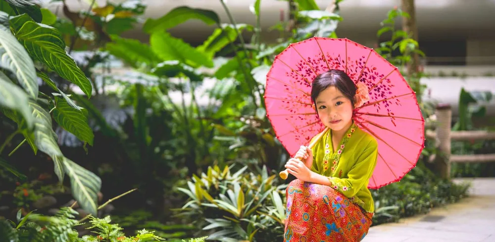 Child in Peranakan kebaya with a pink parasol in the gardens of Shangri-La Singapore